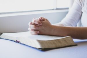 Hands folded in prayer over an open Bible during a church prayer line